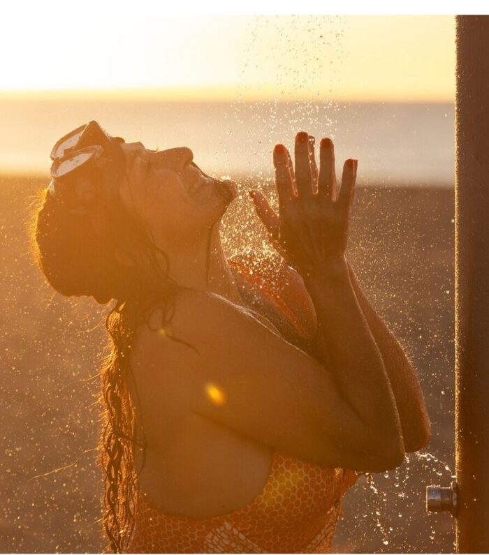 Vrouw geniet van zonlicht onder de douche, wat een positieve uitstraling van vitamine D en zonblootstelling symboliseert.